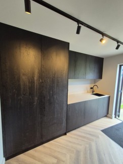 Bijkeuken in donker houtdecor met stenen blad en zwarte spoelbak